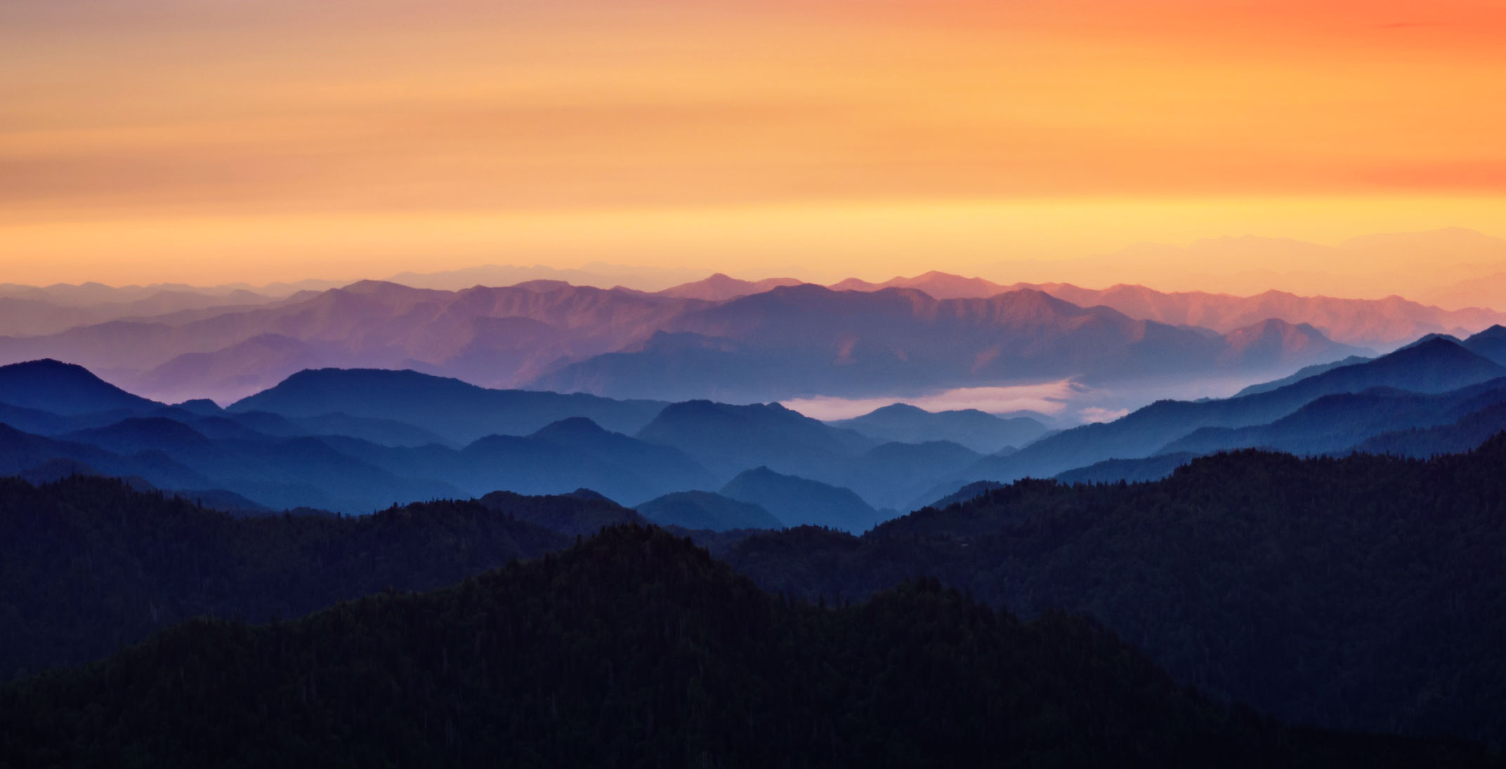 large blue mountains with an orange sunset sky